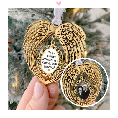 Ornamento dourado com asas e texto a uma face, fotografia a outra, pendurado em árvore de Natal