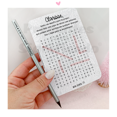 Mão segurando lápis prateado e folha com sopa de letras