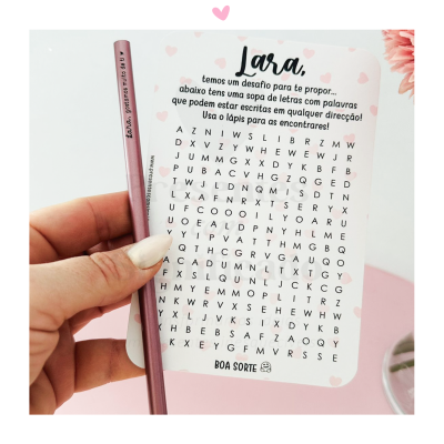 Cartão com puzzle de sopa de letras personalizado e lápis rosa contra fundo branco com decoração floral.