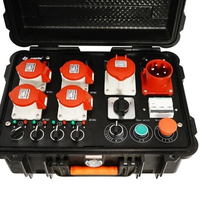 Caixa preta com painel elétrico e conectores industriais vermelhos e brancos em fundo branco.