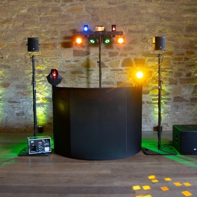 Equipamento de DJ com colunas, mesa e iluminação contra parede de pedra