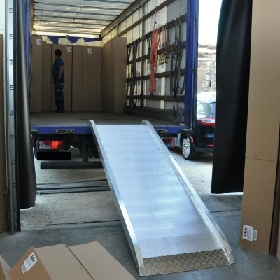 Rampa metálica prateada na traseira de camião aberto com caixas de cartão castanhas ao redor