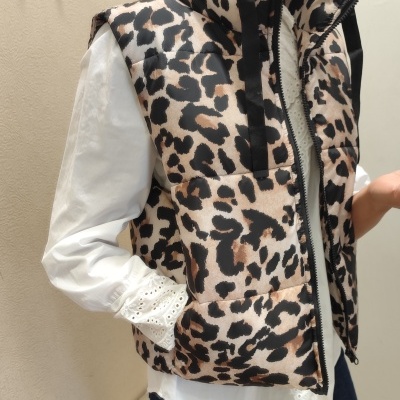Colete acolchoado animal print castanho e preto com fecho, camisa branca bordada e ambiente interior claro