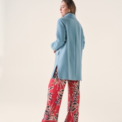 Mulher de casaco azul claro e calças largas vermelhas com padrão floral