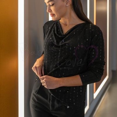 Mulher a usar blusa preta com lantejoulas e calças pretas em corredor iluminado