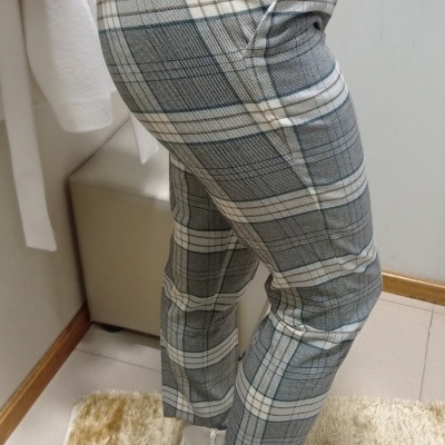 Calças às riscas cinza, branco e bege, bolso lateral com fecho, usadas com botins brancos e camisola verde