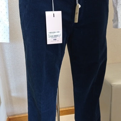 Calças de veludo azul escuro com cinto castanho e camisa branca em manequim