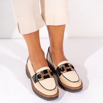Sapatos mocassim bege claro e preto com acessórios dourados, usados com calças bege claras