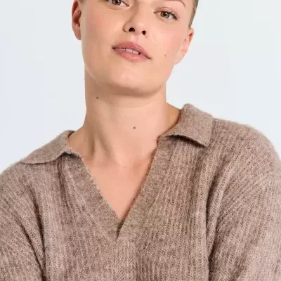 Mulher com camisola castanha de malha com gola aberta sobre fundo branco.