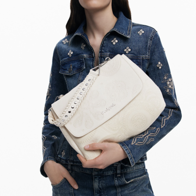 Mala branca floral da Desigual com alça tachas, segurada por modelo com roupa azul de ganga bordada