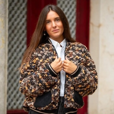 Casaco peludo padrão castanho e preto com bolsos e punhos pretos usado por mulher diante de porta vermelha