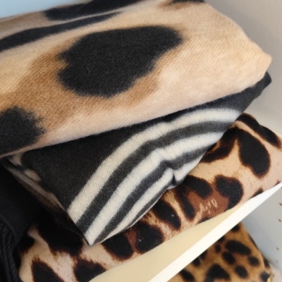 Cachecóis com padrões de pele de animal dobrados numa prateleira branca