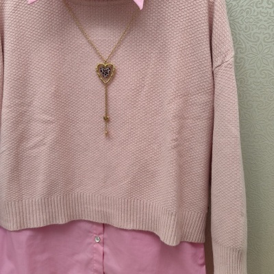 Conjunto de camisa rosa com camisola rosa clara e colar dourado em fundo decorativo