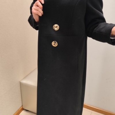 Casaco comprido preto com botões dourados e gola alta.