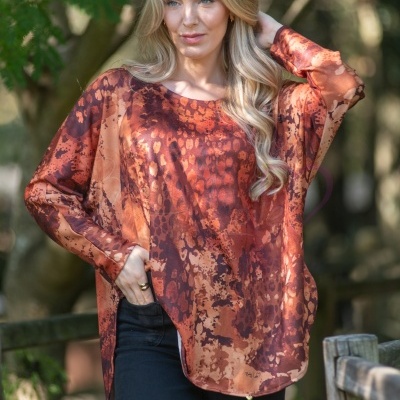 Túnica feminina com padrão abstrato castanho e laranja e calças pretas num ambiente exterior