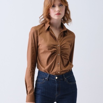 Blusa castanha franzida com botões e jeans escuro num fundo branco