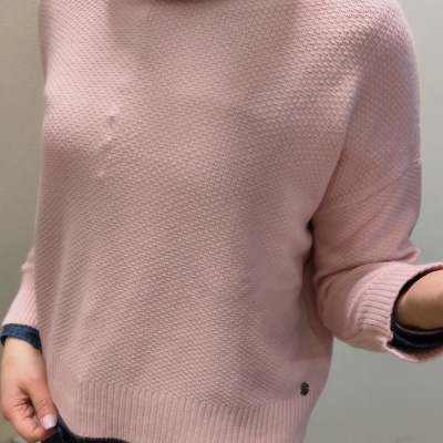 Camisola de gola alta rosa claro com padrão texturizado usada sobre camisa azul escura.