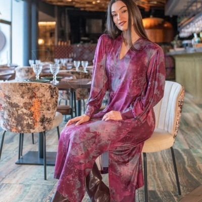 Mulher sentada com vestido vinho e cinza e botas castanhas num restaurante elegante