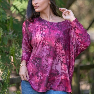 Mulher vestindo túnica rosa e roxa com padrão abstrato com calças de ganga em ambiente natural