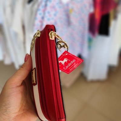 Carteira vermelha e branca com fechos dourados e etiqueta 'Cavalinho' em loja de roupas.