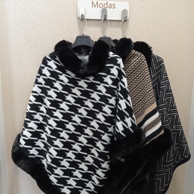 Três ponchos em padrões preto, branco, bege e cinza com detalhes em pele, pendurados numa parede com o texto Prince Modas.