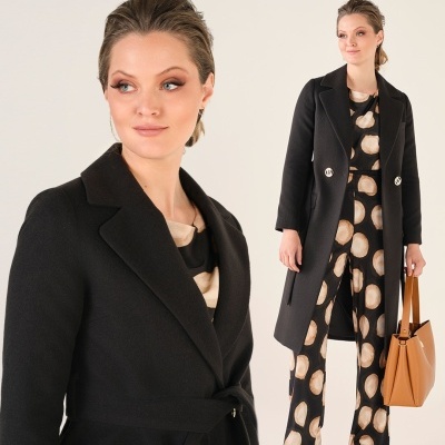 Mulher com casaco preto comprido, calças e blusa pretas com padrão de círculos bege, e mala castanha.