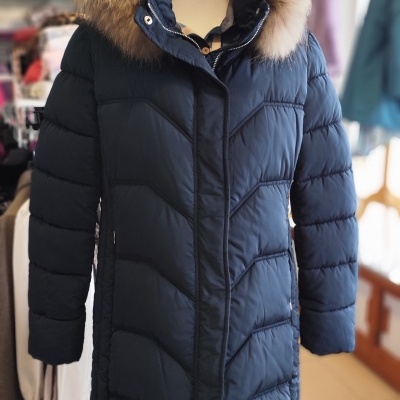 Casaco acolchoado preto com capuz de pelo castanho, em manequim dentro de loja