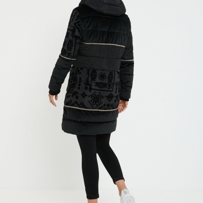 Mulher vista de costas com casaco preto comprido com capuz e padrão floral preto, leggings pretas e sapatilhas brancas.