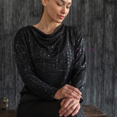 Blusa feminina preta com brilhos e calças pretas sentada em superfície de madeira