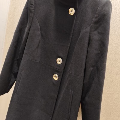 Casaco preto com botões amarelos pendurado num cabide preto