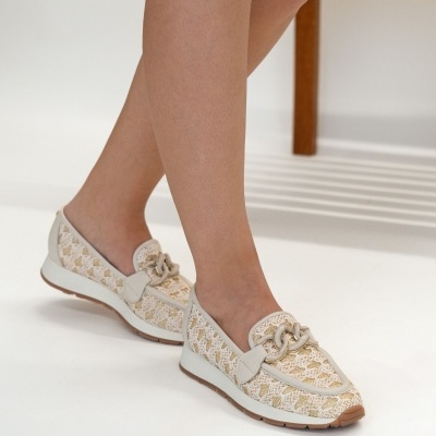 Mocassins femininos bege e branco com detalhe metálico castanho em ambiente interior.