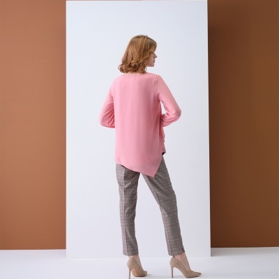 Mulher de costas com blusa rosa assimétrica e calças xadrez cinzentas com salto alto