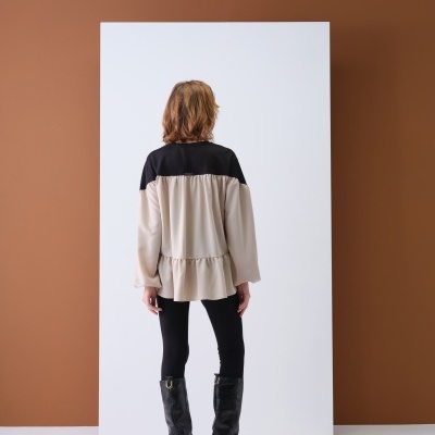 Blusa feminina bicolor bege e preta vista de costas, com leggings pretas e botas pretas de salto médium.