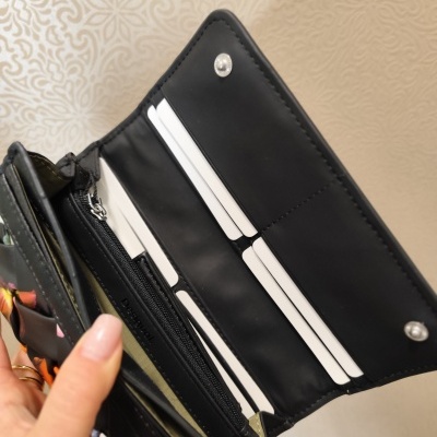 Carteira preta aberta mostrando compartimentos para cartões e moedas, segurada por mão