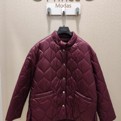 Casaco acolchoado vinho com botões dourados e bolsos pendurado num cabide numa loja com parede estampada.