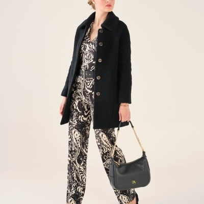 Mulher com casaco preto e roupa com padrão abstrato a segurar mala preta