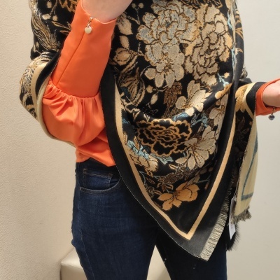 Estola preta com padrão floral bege e dourado com pelo preto usada sobre camisa laranja e jeans azul escuro