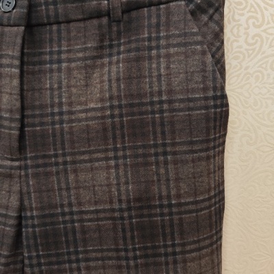 Calças xadrez castanhas e pretas com etiqueta FÁTIMA VERÍSSIMO penduradas num cabide