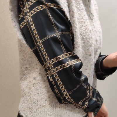 Colete bege de malha com camisa preta de padrão dourado e calças bege