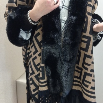 Poncho bege e preto com padrão geométrico e franjas, gola e punhos em pelo sintético preto.