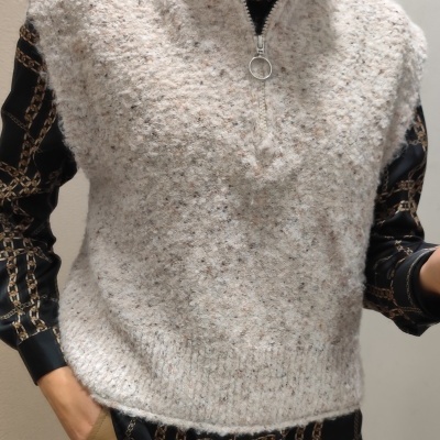 Colete de malha bege com zíper, camisa preta com padrão de correntes e calças castanhas