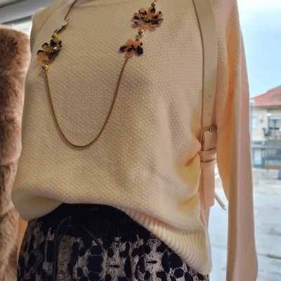 Manequim com camisola creme de gola alta, saia animal print e colar dourado com flores.