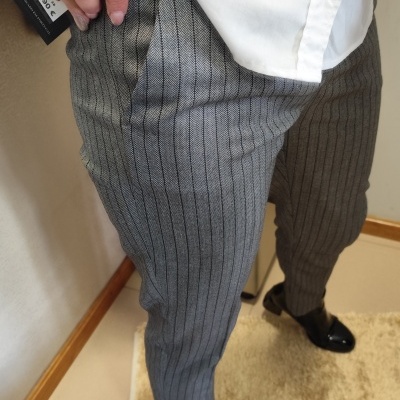 Calças cinzentas às riscas verticais, t-shirt branca e sapatos pretos verniz com etiqueta de preço.