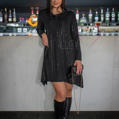 Mulher com vestido preto brilhante e botas pretas junto a balcão de bar