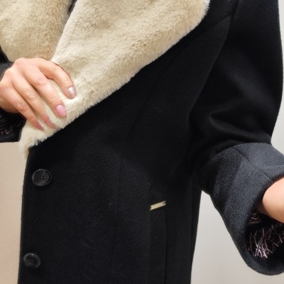 Casaco comprido preto com gola de pelo sintético creme num ambiente interior