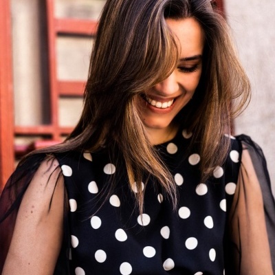 Mulher com vestido preto de bolinhas brancas com mangas transparentes e cabelo castanho claro sorrindo