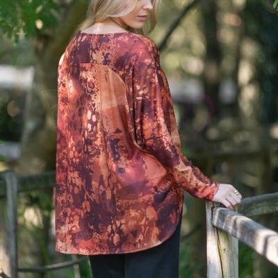 Mulher com túnica de padrão castanho e laranja vista de costas em ambiente natural