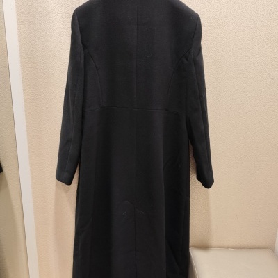 Casaco preto pendurado em cabide contra parede bege texturizada