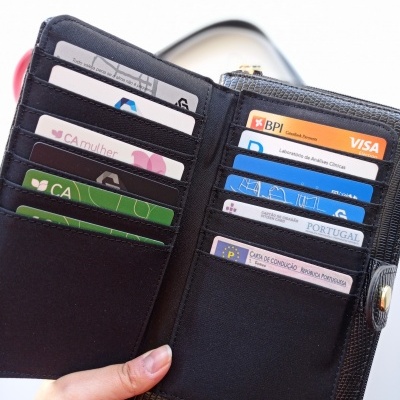 Carteira preta com vários cartões visíveis e mão segurando