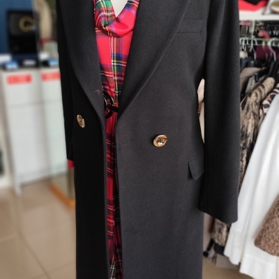 Casaco preto comprido com botões dourados sobre vestido xadrez vermelho em manequim